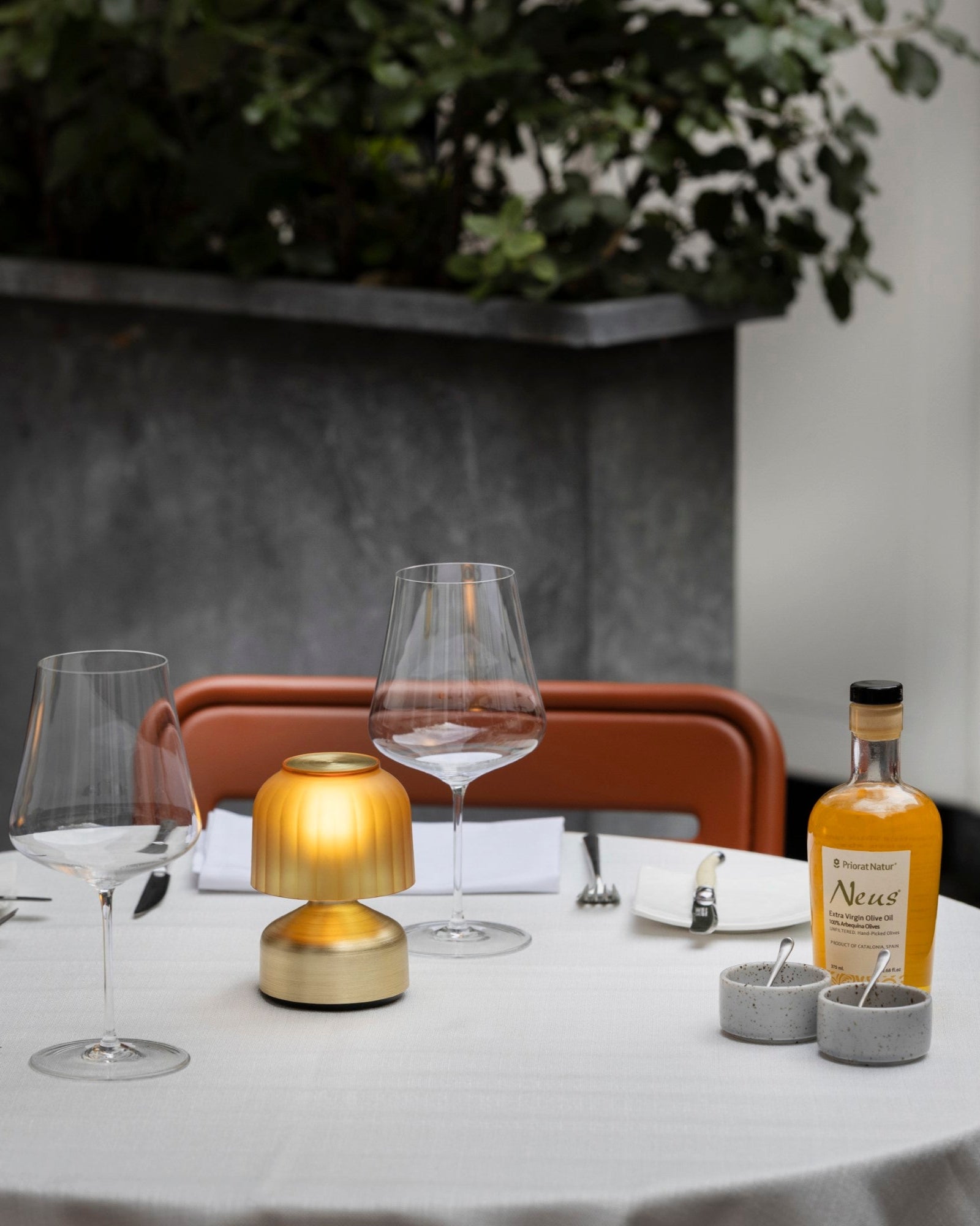 Dining table set with glasses, a bottle, and a small lamp in an outdoor setting.